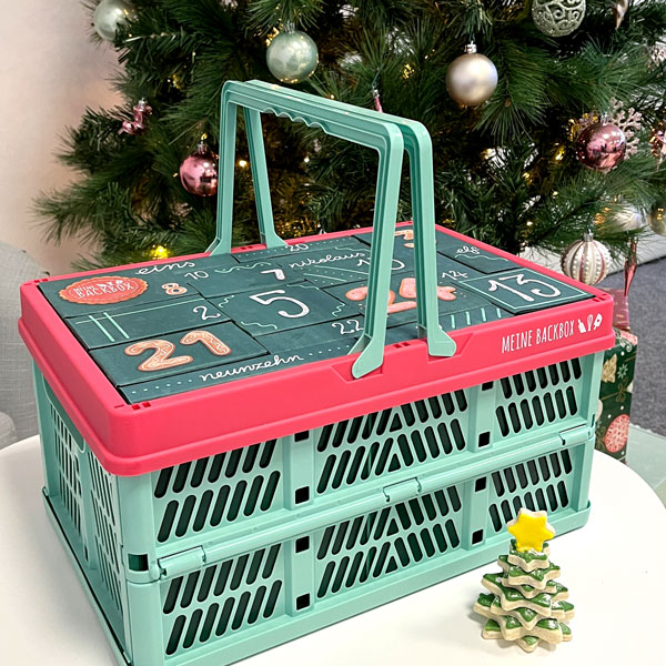 Back Adventskalender 2025 von Meine Backbox im praktischen Einkaufskorb vor einem geschmückten Tannenbaum